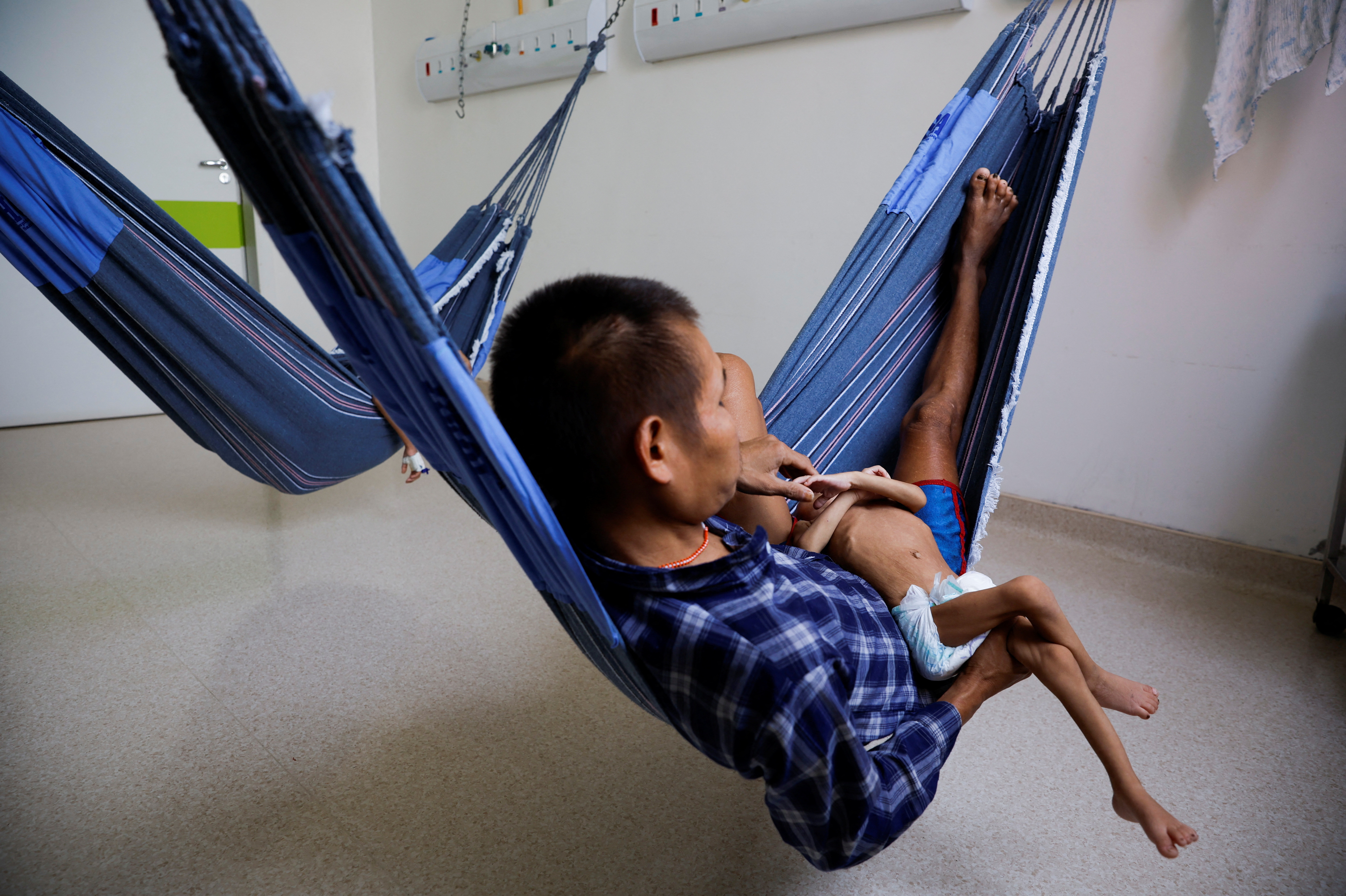 Un niño indígena yanomami de cuatro años, que recibe tratamiento por desnutrición, sostiene la mano de su padre en el patio especial para indígenas del Hospital Infantil Santo Antonio, en Boa Vista, estado de Roraima, Brasil, 27 de enero de 2023 (REUTERS)