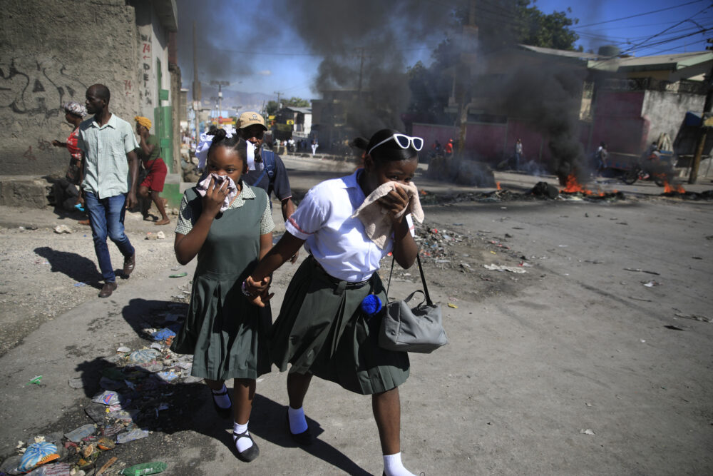 Estudiantes pasan junto a una barricada en llamas levantada por policías que protestan por la mala gestión del departamento, en Puerto Príncipe (AP Foto/Odelyn Joseph)