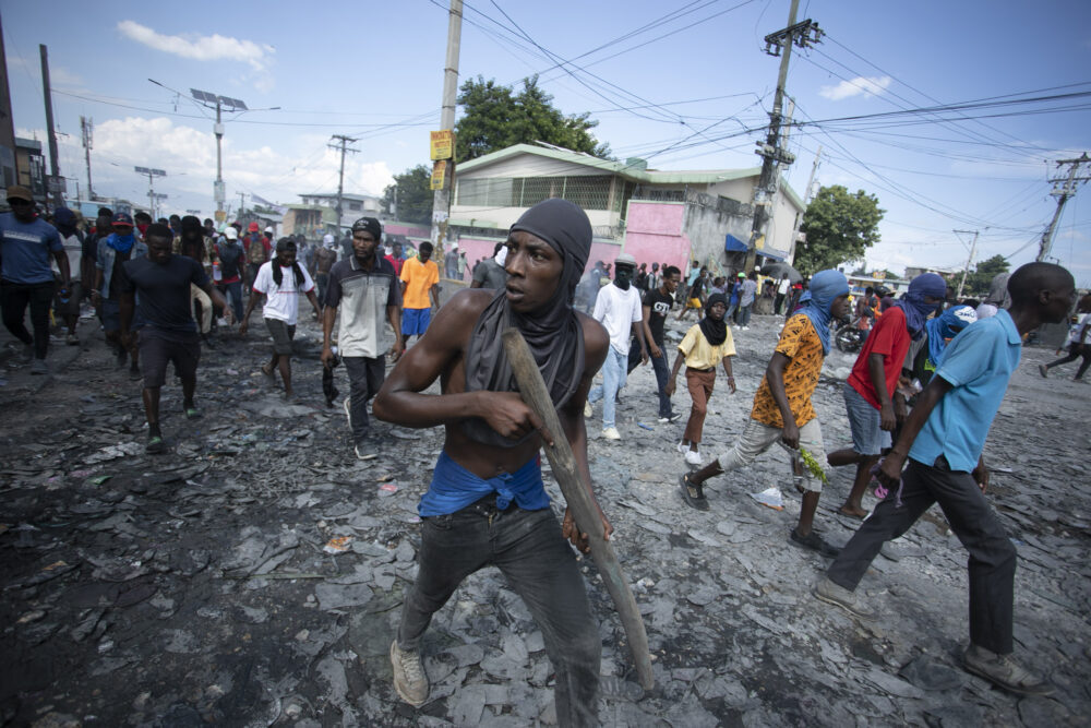 Un manifestante lleva un trozo de madera que simula un arma  (AP Foto/Odelyn Josph)