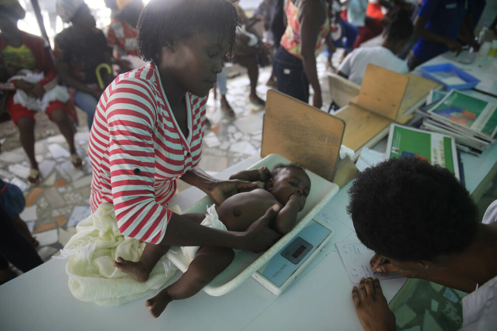 Un trabajador de salud pesa a un niño en el Centro Hospitalario de Fontaine, donde el bebé recibió múltiples vacunas durante la visita en el área de Cité Soleil de Puerto Príncipe, Haití, el lunes 23 de enero de 2023.  (AP Photo/Odelyn Joseph)

