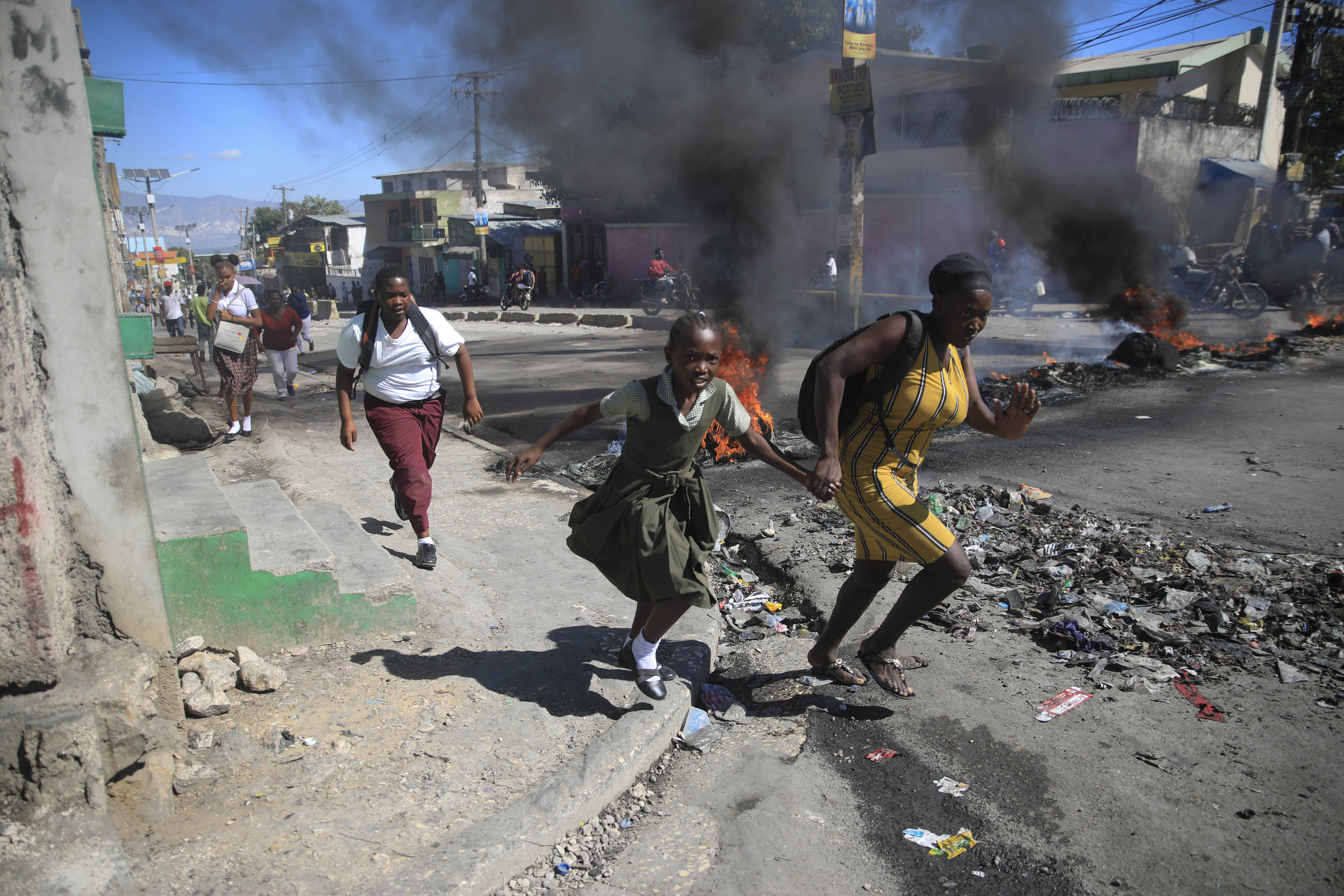 Una mujer y su hija pasan corriendo frente a una barricada levantada por la policía en protesta por el mal gobierno policial en Puerto Príncipe el 26 de enero de 2023 (AP Foto/Odelyn Joseph, Archivo)