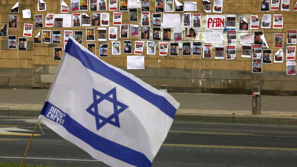 Una bandera israelí ondea frente a un muro con imágenes de personas secuestradas en su ataque del 7 de octubre por el movimiento palestino Hamás, el 16 de octubre de 2023 en Tel Aviv, en el exterior del Ministerio de Defensa israelí