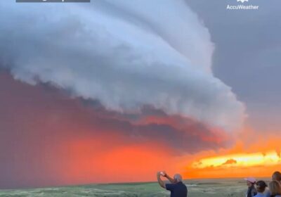 | Una puesta de sol naranja detrás de una supercélula imponente mientras los relámpagos…